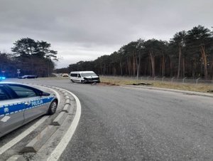 na pierwszym planie radiowóz z włączonymi sygnałami świetlnymi, na drugim planie biały bus uczestniczący w zdarzeniu i przewrócona latarnia