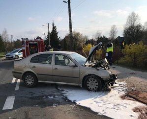 Miejsce wypadku drogowego. Na pierwszym planie uszkodzony skoda, na drugim planie wóz strażacki i radiowóz policyjny.