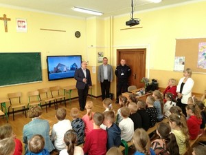 od lewej dyrektor szkoły, prowadzący zajęcia, policjant oraz tyłem uczniowie podczas spotkania