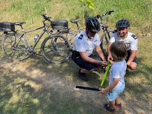 Policjanci z patrolu rowerowego wręczający opaskę odblaskową chłopcu.